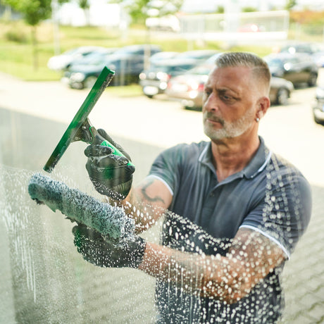 Ein Mann putzt Fenster mit UNGER Werkzeugen