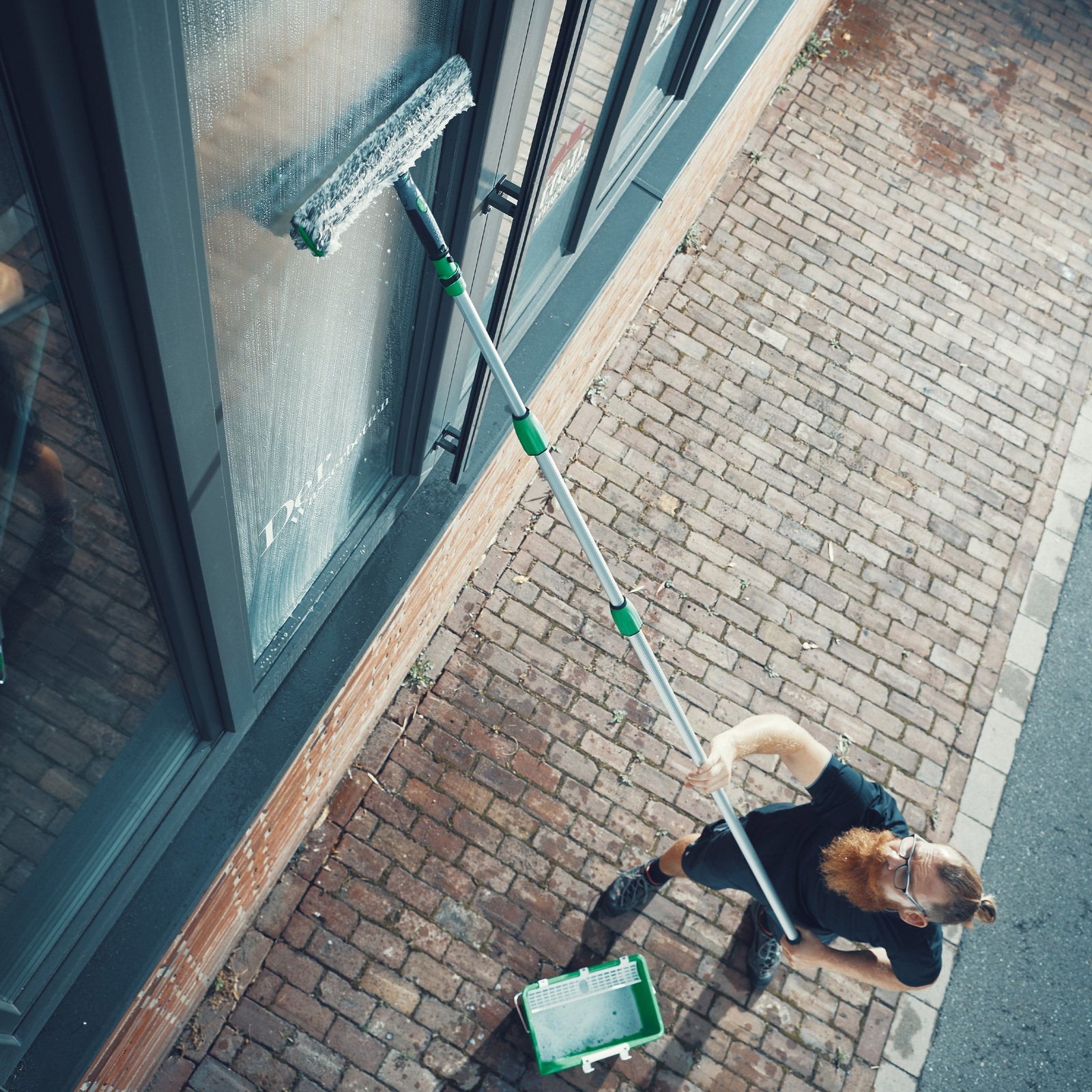 Ein Mann reinigt ein fenster mit einer Teleskopstange und Profi Glasreinigungszubehör
