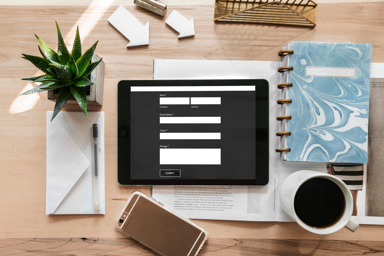 Tablet mit Online-Formular auf Schreibtisch mit Notizbuch, Kaffeetasse und Pflanze.